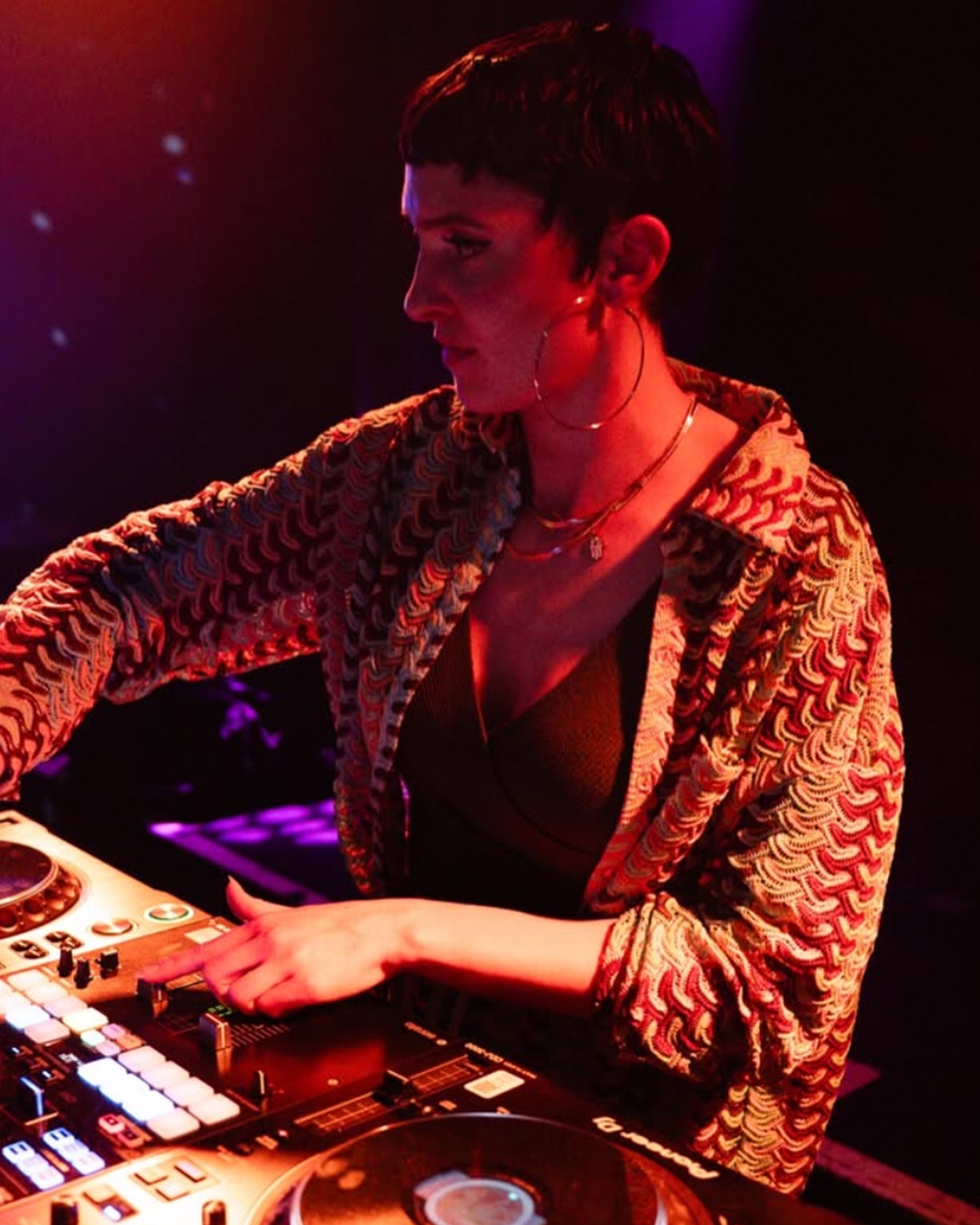 Portrait of DJ SamSam at the controller in warm red club light.